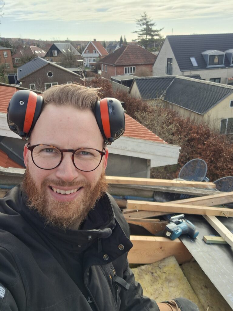 Tømrermester Thomsen sidder på et tag med høreværn under tagrenovering.